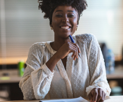 Portrait of woman smiling, holding pen to chin.