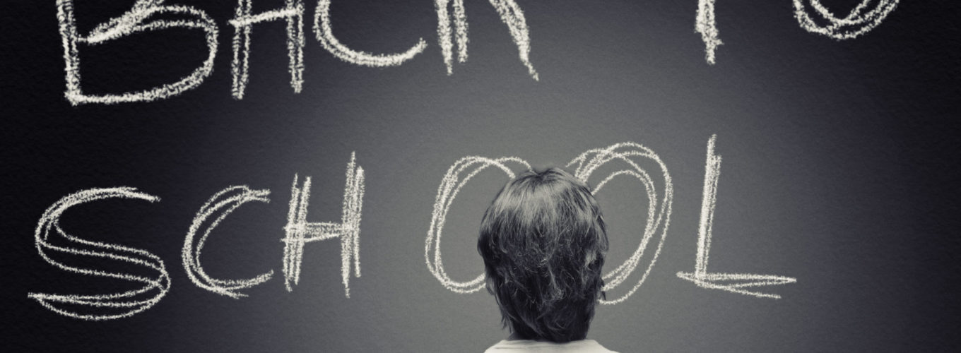 Man in t-shirt is staring at a huge blackboard with "BACK TO SCHOOL" handwritten with chalk on it