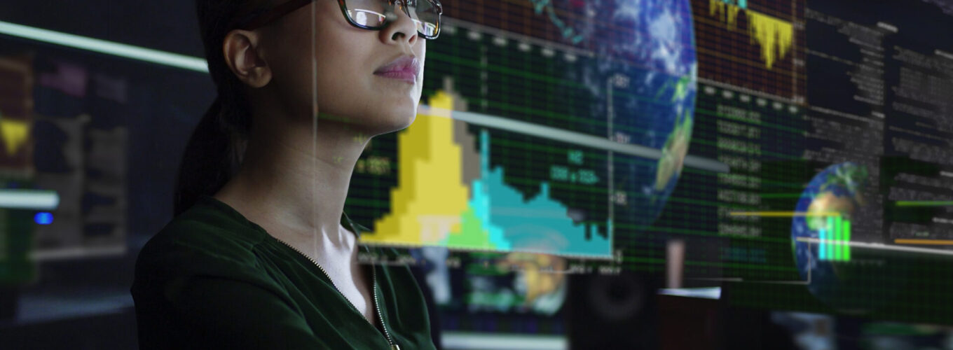 A young Asian woman looking at see through employment and higher education retention data whilst seated in a dark office. The data is projected on a see through (see-thru) display.
