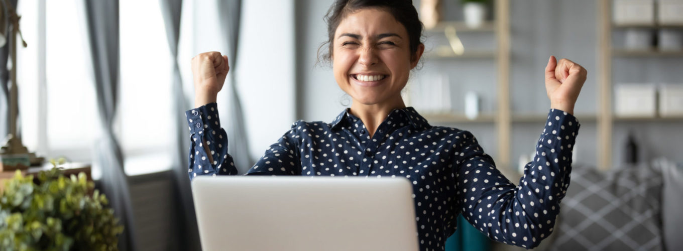 Euphoric young indian girl student winner celebrate victory triumph sit at home desk with laptop computer win online fortune feel excited get new job opportunity good exam result great news concept