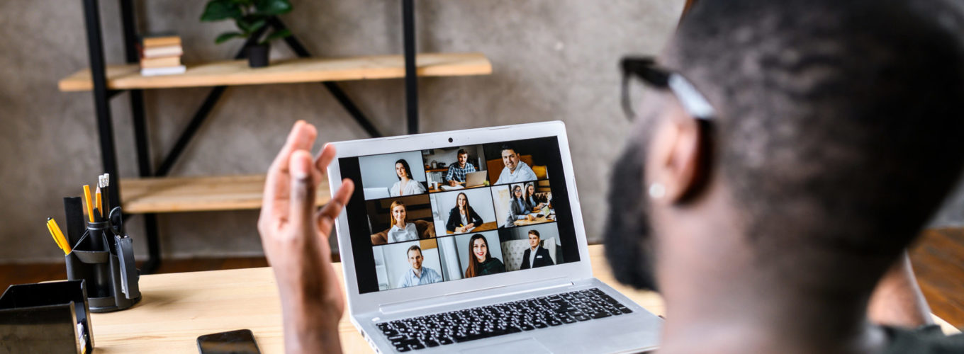 Confident African-American male worker talking online with an online class, back view of black man speaks and gestures to many people on video screen. Remote education, virtual meeting