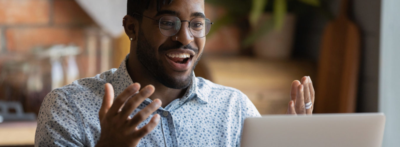 Happy young afro american man software developer run program code on pc enjoy reaching successful result. Overjoyed black guy look on laptop screen splash hands having winning hand at online blackjack