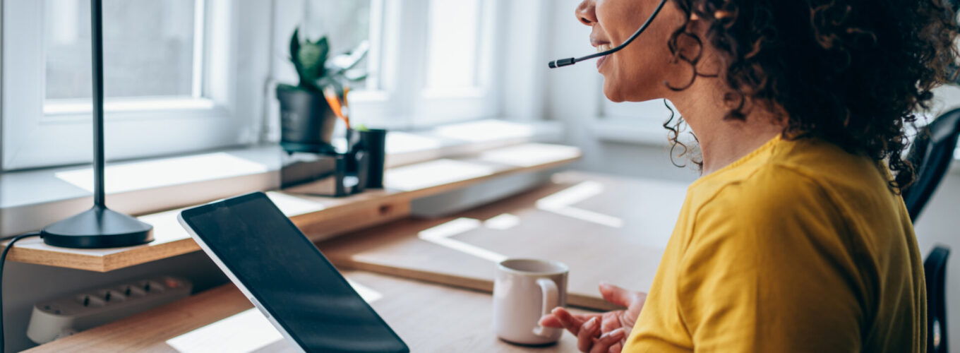 Shot of a young woman using a digital tablet and headset while working from home. Beautiful young woman having video call in the office. Shot of an attractive woman using a tablet for video conference.