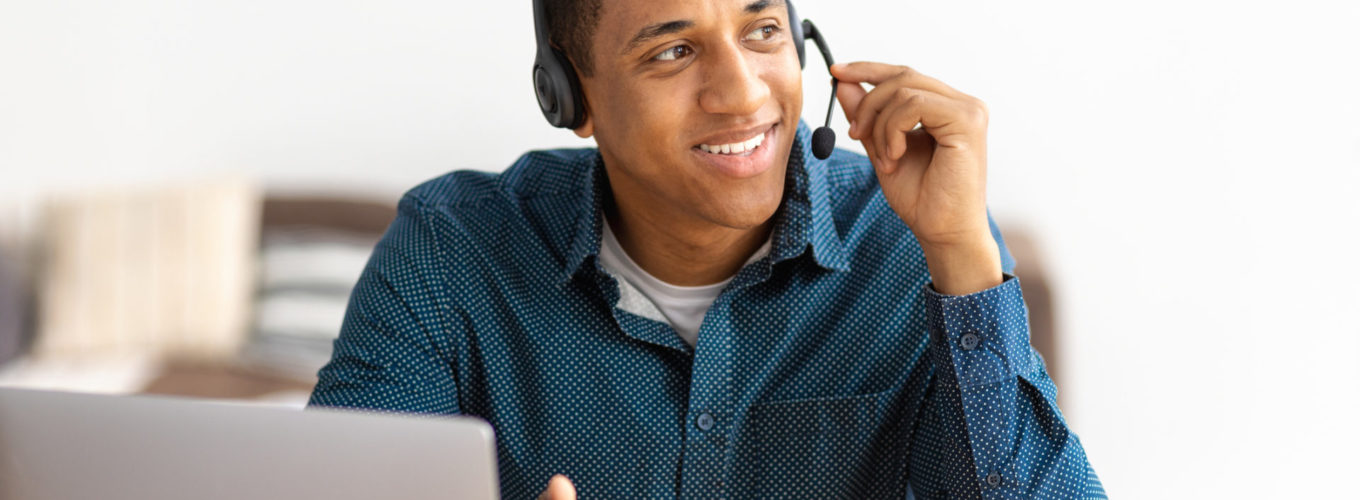 Successful mixed race man in headset, student support specialist sitting in a modern office and talking to a student, smile