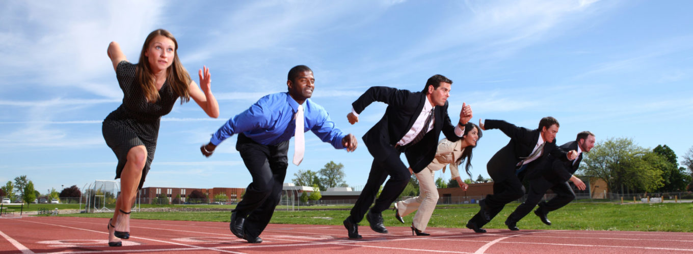 Group of people dressed in business attire racing on track.  Some slight motion blur on people.