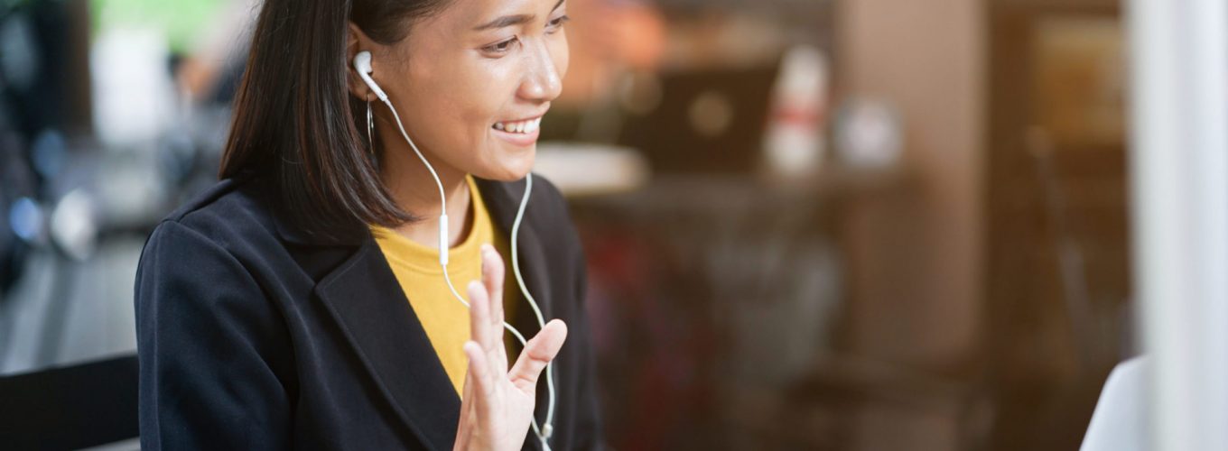 close up asian woman use earphone connect to laptop and talking greeting by video conference with friends or family at outdoor coffee restaurant in relax time , lifestyle people concept