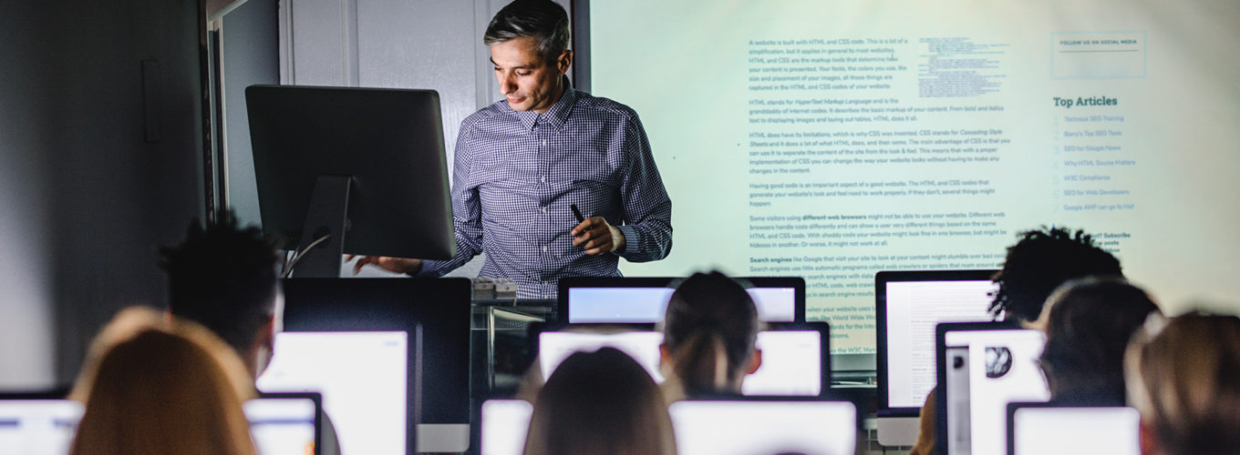 Male teacher giving a lecture from desktop PC during a class at computer lab.