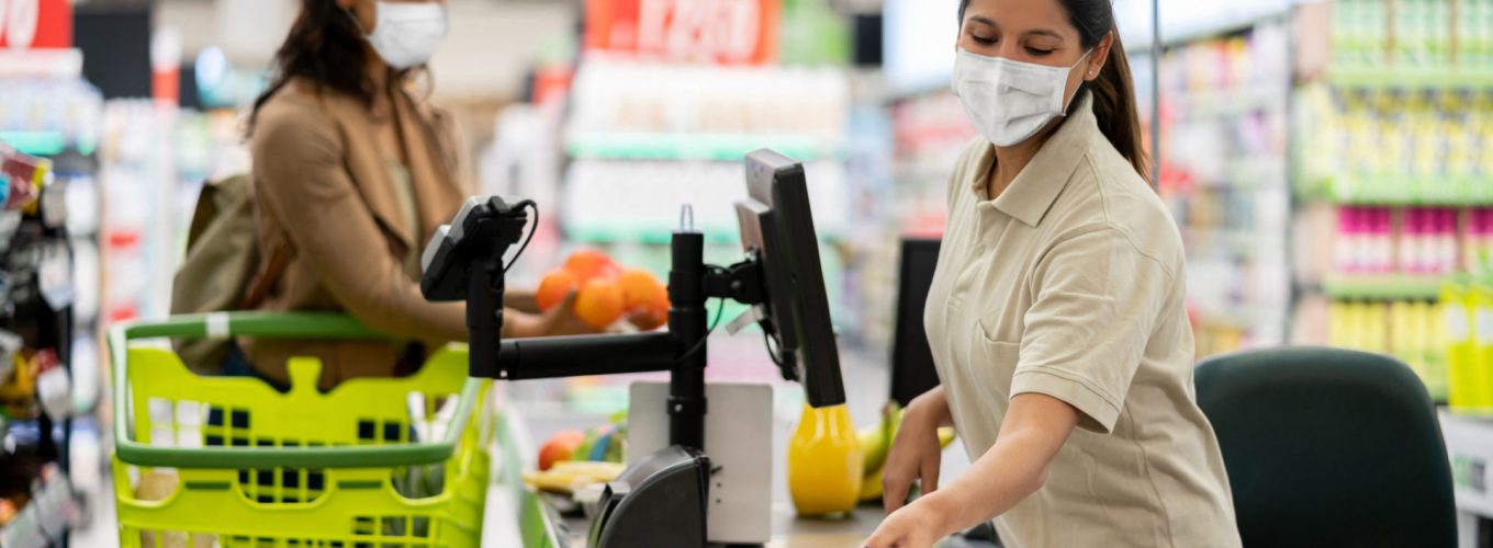 Latin American cashier scanning products at a grocery store wearing a facemask - quarantine lifestyle concepts