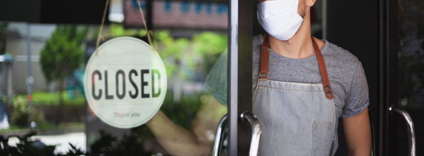 Chef in safety mask hanging up sign closed on restaurant door.